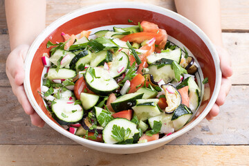 Kids hands holding vegan salad on wooden background