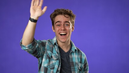 Fototapeta premium Portrait of happy smiling young man 20s smiling waving at friend meet greet with hand as notices someone isolated on purple background.