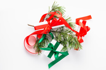 Two gift boxes with red and green ribbons, and pine cone twig over white background, top view