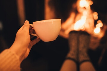 Woman drinkink hot cocoa sitting by the fire in front of cozy fireplace.