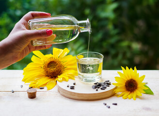 Sunflower oil pouring from the bottle into a glass with sunflowers and seeds on background