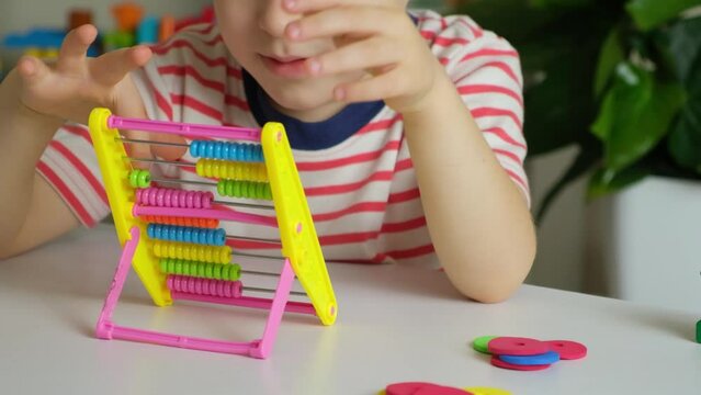 A 5-year-old boy is learning to count on abacus, mathematics, arithmetic for preschoolers.