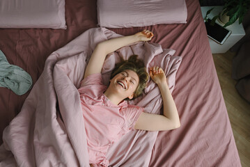 Happy young girl lies on the bed and laughs. Carefree teenager enjoying the weekend. View from above