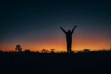 Silhouette im Abendrot - Kind reckt vor atemberaubender Sonnenuntergangskulisse seine Arme in den Himmel, Quiver tree Forest, Namibia
