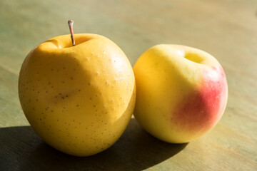 Yellow apples closeup indoor lit by sunlight on green wooden surface