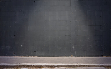Frontal view of a black brick wall at night. In the foreground is a sidewalk illuminated by a cone...