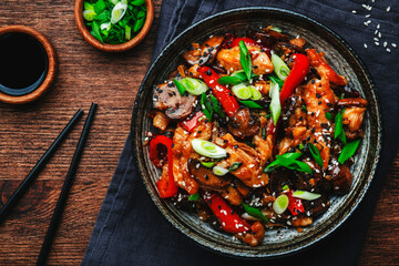 Stir fry chicken with paprika, mushrooms and chives in bowl. Asian cuisine dish. Wooden kitchen table background, top view
