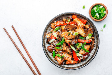 Stir fry with turkey fillet, red paprika, mushrooms, green chives and sesame seeds in bowl Asian cuisine dish. White kitchen table background, top view