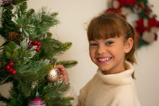 Ni&ntilde;a decorando el &aacute;rbol de navidad con una gran sonrisa 