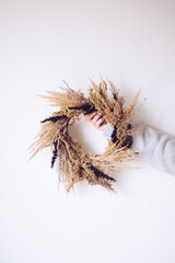 Stylish autumn wreath. Hands holding dry grass, wildflowers and wheat rustic wreath