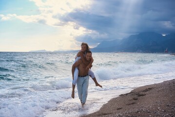Fototapeta na wymiar Happy couple in love on beach summer vacations. Joyful girl piggybacking on young boyfriend having fun.