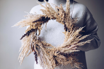 Stylish autumn wreath. Hands holding dry grass, wildflowers and wheat rustic wreath