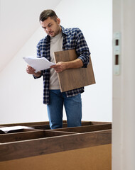 Man assembles furniture at home looking assembly instruction manual.