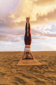 Beautiful woman practicing yoga on the beach at sunset, doing headstand exercise, salamba sirsasana