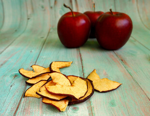 a few chips from dried apples lie on a blue wooden background against the background of three juicy red apples front view.  food