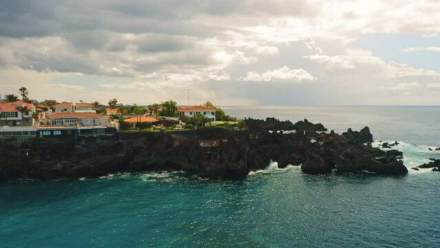 Aerial view of natural ocean coastline with pool on rocky volcanic beach of Devil in Tenerife Canary Island. Charco El Diablo. Black frozen lava flows volcanic bizzare stones. Resort town cityscape.