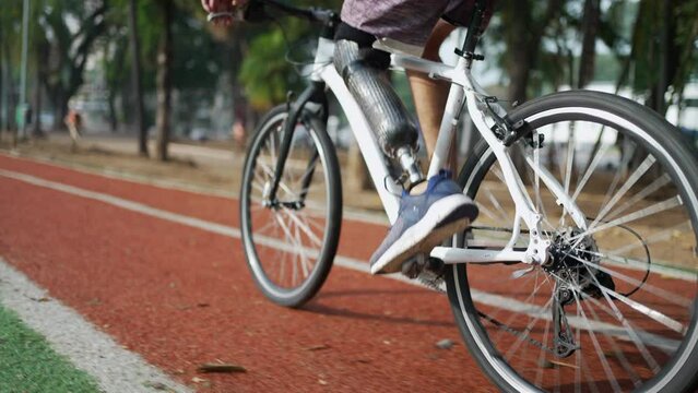 Disabled person riding bicycle using prosthetic leg outdoors