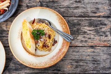 Top view of Spaghetti Carbonara with crispy ham and white cream sauce in ceramic plate on wooden table