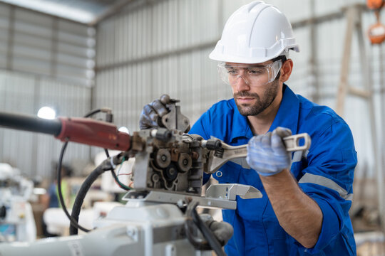 Male Engineer Using Wrench Tool Repair Robot Arm Welding Machine In Factory. Technician Automation Robot In Uniform Working At Robot Industrial.