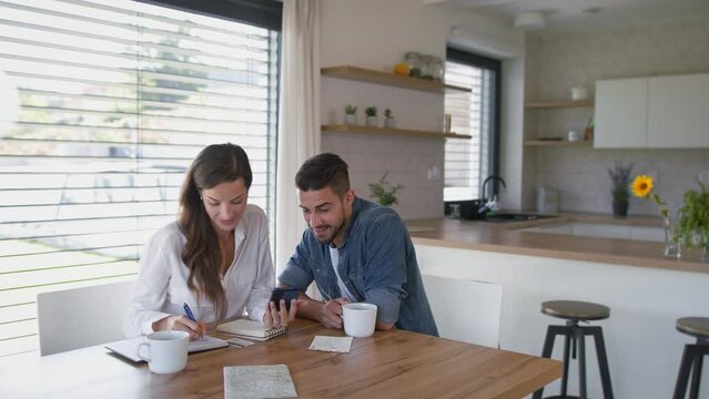 Young couple at home, using mobile phone for planning of finances.
