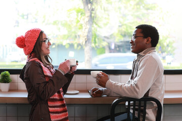 Fototapeta premium Two young couples, girl friends in sweaters standing in a cafe smiling talking concept of living people