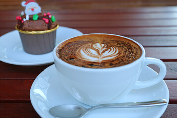 A Cup of Hot Cappuccino Coffee with Blurry Christmas Cupcake in the Backdrop