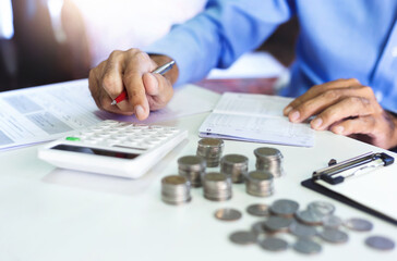 Asian businessman on desk in office using calculator to calculate saving account passbook and statement with financial report. concept of saving for the future and family , close-up view