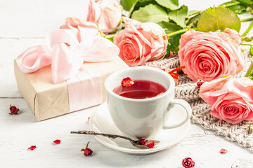 The concept of romantic tea. Wrapped gift, hibiscus tea, a bouquet of delicate roses, sweets