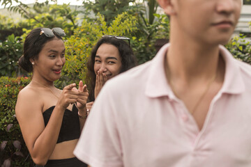 Two young women talk behind a unsuspecting man's back. Ladies spreading slanderous rumors. Outdoor...