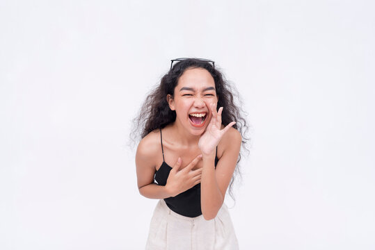 A young excited woman screams from the top of her lungs. Covering her mouth with one hand. Isolated on a white backdrop.