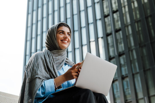 Young muslim woman wearing headscarf using cellphone and laptop outdoor