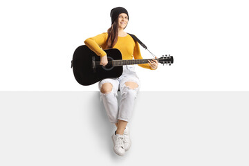 Young female musician playing an acoustic guitar and sitting on a blank panel