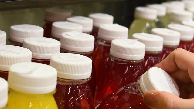 Woman Hand Selects Fresh Squeezed Juice In Plastic Bottle of different colors, filled with vitamins from different fruits and vegetables At Supermarket. Closeup.