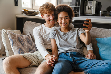 Young happy interracial couple taking selfie with phone together