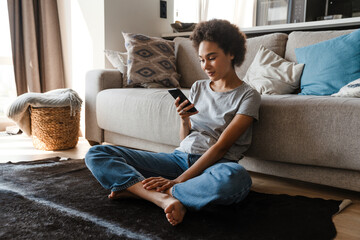 Young beautiful smiling curly african woman holding and using phone