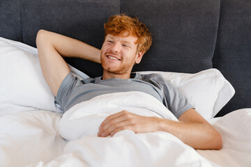 Young handsome smiling redhead man in gray t-shirt looking aside