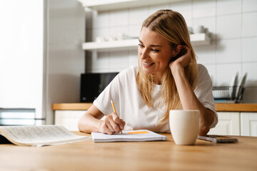 Blonde white woman drinking coffee while doing homework in kitchen