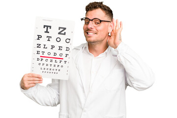 Young caucasian oculist man isolated trying to listening a gossip.