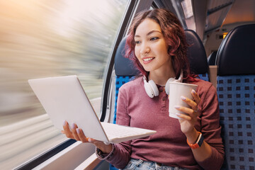 Happy young girl rides in a modern intercity train and remotely via Wi Fi Internet works or studies...