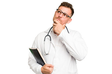 Young doctor caucasian man holding a book isolated looking sideways with doubtful and skeptical...