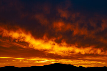 The beautiful colors of the clouds during sunrise over hills in silhouette
