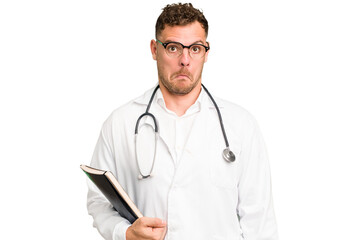 Fototapeta premium Young doctor caucasian man holding a book isolated shrugs shoulders and open eyes confused.