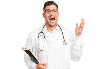 Young doctor caucasian man holding a book isolated receiving a pleasant surprise, excited and raising hands.