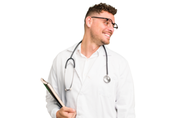 Young doctor caucasian man holding a book isolated looks aside smiling, cheerful and pleasant.