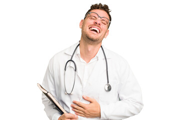 Young doctor caucasian man holding a book isolated laughing and having fun.
