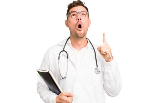 Young doctor caucasian man holding a book isolated pointing upside with opened mouth.