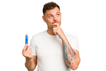Young caucasian man holding a electronic cigarette isolated relaxed thinking about something looking at a copy space.