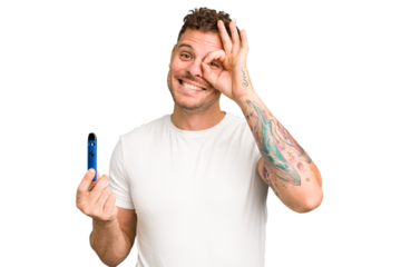 Young caucasian man holding a electronic cigarette isolated excited keeping ok gesture on eye.