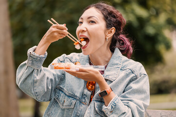 A girl has lunch and snacks on traditional Japanese sushi in the park after a working day. Cuisine and diet concept