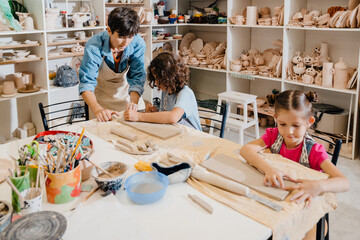 Mature female teacher making pottery crafts with group of kids at workshop